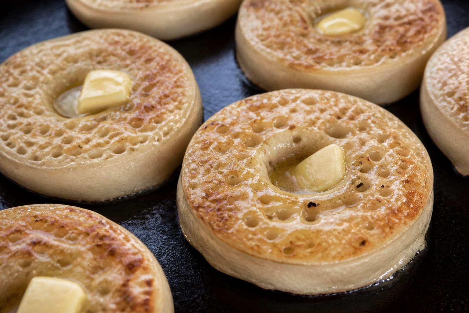 Gluten-free sourdough crumpets on a griddle showing classic surface holes